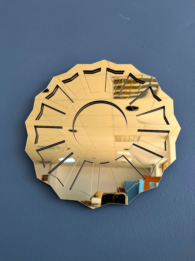 May include: A gold-colored, round mirror with a geometric design. The mirror has a sunburst pattern with 12 points.