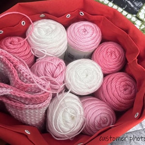 May include: A red fabric bag filled with pink and white yarn balls. The bag has a drawstring closure and is made of a soft, durable material.