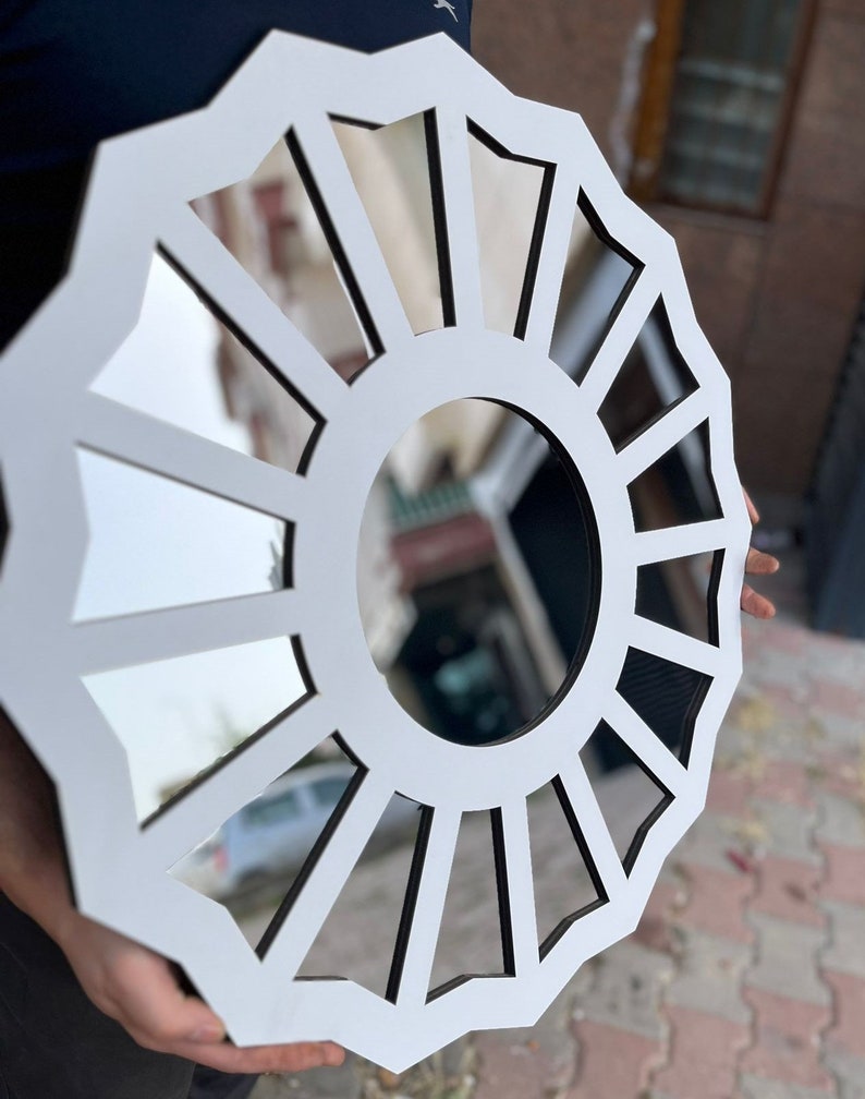 May include: White round mirror with a black frame and a sunburst design. The mirror is divided into 16 sections, each with a slightly different shape.