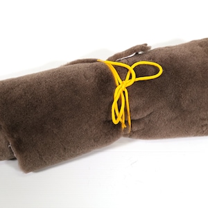 Op de afbeelding: Een bruin nep bont deken opgerold en vastgebonden met een geel touwtje.