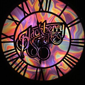 May include: A black clock with Roman numerals and a colorful, swirling background. The clock face features the text "Blackberry Smoke" in a stylized font.