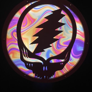 May include: A circular wooden wall hanging with a psychedelic swirl pattern and a black silhouette of the Grateful Dead's iconic lightning bolt skull logo.