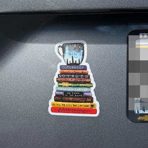 May include: A sticker featuring a stack of books topped with a mug showing a starry night sky. The book spines are labeled with titles including Outlander, Voyager, Drums of Autumn, An Echo in the Bone, Go Tell the Bees That I Am Gone, and A Blessing.