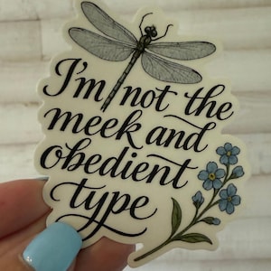 May include: A sticker with a dragonfly illustration and the text "I'm not the meek and obedient type." The design includes blue forget-me-nots and is in a whimsical font.