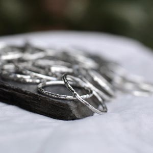 May include: A stack of silver hammered rings on a grey stone surface. The rings are thin and have a textured finish.