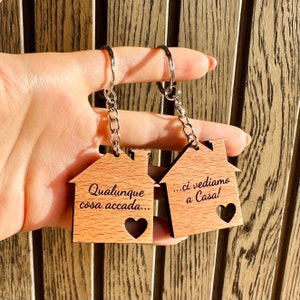 K&ouml;nnte beinhalten: Zwei Schl&uuml;sselanh&auml;nger aus Holz in Form eines Hauses mit einer silbernen Kette. Der Schl&uuml;sselanh&auml;nger links sagt "Qualunque cosa accada..." und der Schl&uuml;sselanh&auml;nger rechts sagt "...ci vediamo a Casa!"