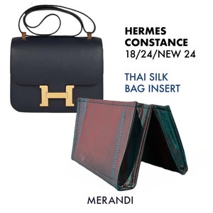 May include: A navy blue Hermes Constance handbag with a gold-colored 'H' clasp and a black strap. Beside it is a Thai silk bag insert in shades of red, green, and blue. The text on the image reads 'HERMES CONSTANCE 18/24/NEW 24', 'THAI SILK BAG INSERT', and 'MERANDI'.
