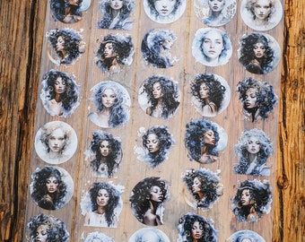 May include: A sheet of circular stickers featuring watercolour portraits of women with various hairstyles. The portraits are in shades of blue, grey, and black, with a watercolour effect. The stickers are on a transparent sheet.