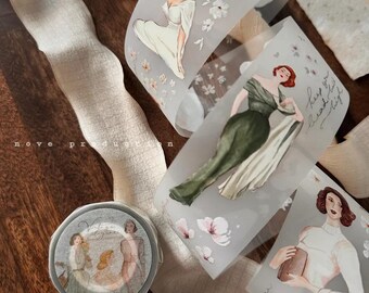 May include: Decorative washi tape featuring vintage illustrations of women in elegant dresses, with floral accents. The tape is partially unrolled, revealing the printed designs. A roll of tape is also visible.