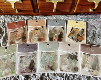 May include: A collection of Clair brand sticker packs, each containing various vintage-themed stickers. The packs feature illustrations of women, teacups, cameras, and other antique elements. The packaging is clear, allowing the stickers to be visible.