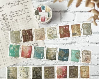 May include: A collection of vintage-style postage stamps in various colors, including green, red, and brown, arranged on a white surface. A roll of washi tape with stamp designs is also present. The stamps feature intricate designs and numbers.