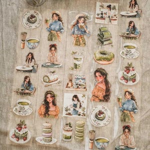 Puede incluir: Una hoja de pegatinas decorativas con ilustraciones de acuarela de mujeres disfrutando de té matcha y pasteles. Las pegatinas incluyen imágenes de pasteles, donuts, macarons y tazas de té. La paleta de colores es suave, con verdes pastel, rosas y marrones.