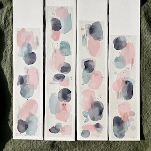 May include: Four watercolor bookmarks with abstract designs. Each bookmark features a white background with overlapping shapes in shades of pink, gray, and teal. The designs have a soft, artistic aesthetic.