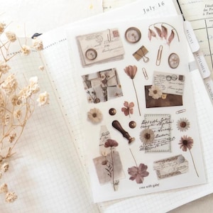 May include: A transparent sticker sheet featuring a collection of vintage-inspired illustrations including envelopes, wax seals, dried flowers, paper clips, and handwritten script notes in muted brown, beige, and cream tones with the text crea with gaby.