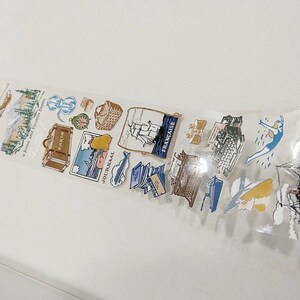 Può includere: Rotolo di nastro washi trasparente con illustrazioni a tema viaggio. I disegni includono una valigia, una barca a vela, un nuotatore e la parola "FRANCAISE". Ideale per scrapbooking e progetti creativi.