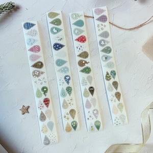 May include: Four rolls of decorative washi tape with tear-drop shaped designs in various colors. Each tear-drop features a different pattern, including stripes, polka dots, and floral motifs. The color palette includes blue, green, pink, and brown.