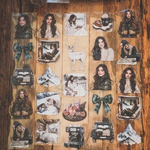 May include: A collection of decorative stickers featuring winter-themed illustrations. The stickers include images of women, deer, mountains, vehicles, bows, and cozy scenes with coffee and books. The stickers are arranged on a wooden surface.