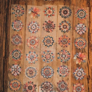 May include: Decorative floral stickers in various sizes and designs. The stickers feature intricate patterns in shades of orange, blue, and brown. The stickers are arranged on a wooden surface, with a roll of stickers visible at the top.
