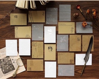 May include: An assortment of vintage-style stationery items, including postcards, notecards, and translucent sheets, arranged on a wooden surface. The color palette includes shades of brown, white, and gray. A magnifying glass, a feather quill, and dried flowers are also present.