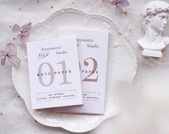 May include: Two small notebooks with the text "Jennyuanzi Studio" and the numbers "01" and "02" on the covers. The notebooks are white with light brown and mauve text. The notebooks are on a white, decorative plate.