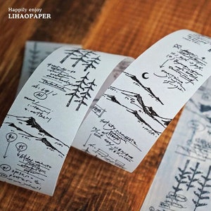 May include: White decorative washi tape with black sketched mountain, tree, and handwritten text designs. The tape features the text "Happily enjoy LIHAOPAPER". The tape is rolled up on a wooden surface.