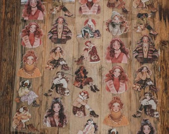 May include: A collection of transparent stickers featuring illustrations of women in various poses and outfits. The stickers showcase a warm colour palette with shades of brown, beige, and red, with some wearing winter clothing. The stickers are arranged on a wooden surface.