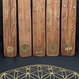 May include: Four wooden incense sticks with gold stars and different designs. The designs include a sun, a yin yang symbol, a meditating Buddha, an Om symbol, and an elephant.