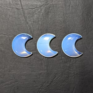 May include: Three iridescent blue crescent moon shaped stones on a black textured surface.
