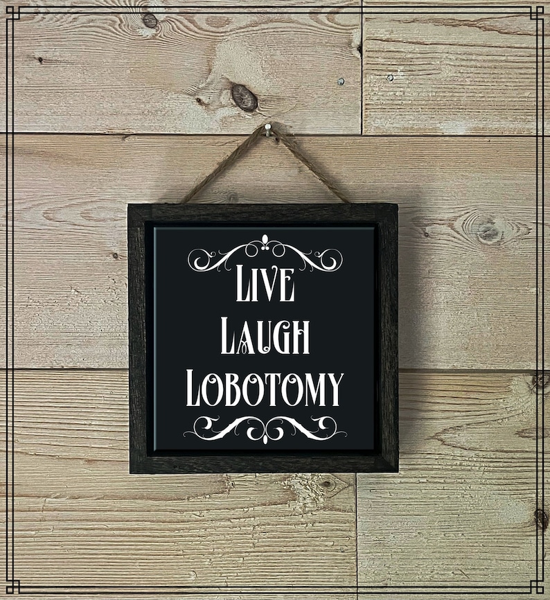 May include: A black framed sign with white text that reads "Live Laugh Lobotomy" on a wood background.
