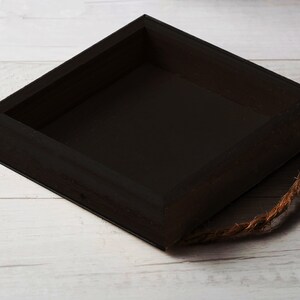 May include: A black wooden box with a rope handle. The box is empty and has a square shape.