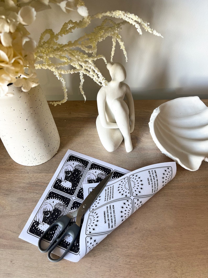 May include: A set of printable tarot cards featuring black and white illustrations of a woman with a crescent moon and stars. The cards are printed on white paper and are being cut with scissors. The text on the cards reads "SOMETIMES TWO SOULS ARE PHYSICALLY TALL APART, MOON THEY NEED TO FALL BACK" and "WHEN SOULS ELECTRICALLY CONNECT VIA THE HEART, TIME AND SPACE DOES NOT HINDER COMMUNICATION."