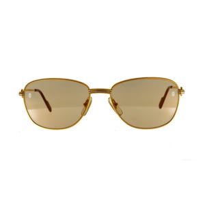 May include: Gold-tone metal sunglasses with a light brown tint. The oval-shaped lenses are set in a thin, gold frame. The temples feature a small, decorative detail. A classic eyewear accessory.