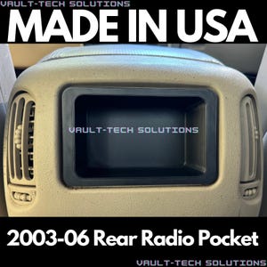 May include: A beige rear radio pocket for a 2003-06 vehicle. The pocket is made of plastic and has a black trim around the opening. The text "VAULT-TECH SOLUTIONS" is printed on the pocket.