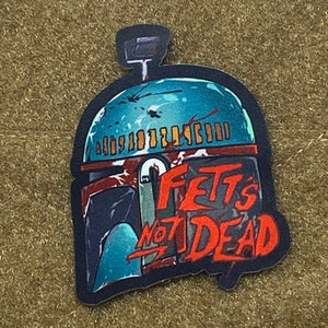 May include: A blue and red sticker with a Boba Fett helmet and the text "Fett's Not Dead".