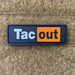 Puede incluir: Parche bordado negro y naranja con el texto "Tac out" en letras blancas.
