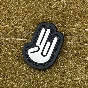 May include: A black and white patch with a hand making the 'rock on' gesture. The patch is made of a soft, textured material and has a white outline.