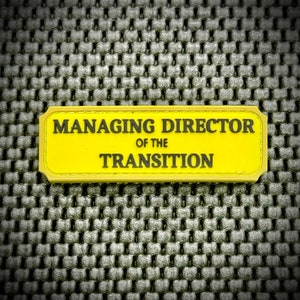 May include: Yellow badge with rounded corners and black text that reads "Managing Director of the Transition".