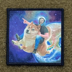 May include: A patch featuring a cartoon Shiba Inu dog wearing a blue shirt and jeans, riding a rocket ship through space. The dog is wearing a blue shirt and jeans. The background is a galaxy with stars and planets.