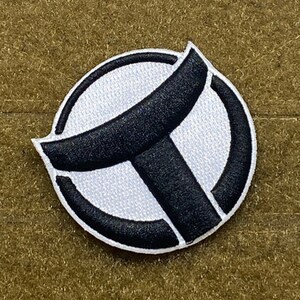 May include: A white and black embroidered patch with a stylized letter "T" inside a circle.