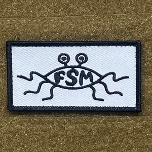May include: White patch with black embroidered image of a cartoon eye with two antennas and the letters FSM inside the eye. The eye has six legs.