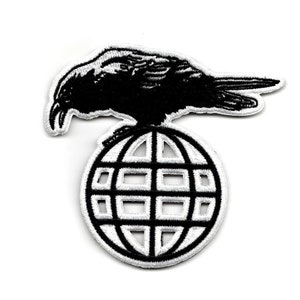 Puede incluir: Parche bordado en blanco y negro de un cuervo posado sobre un globo terráqueo. El cuervo está mirando hacia la izquierda y tiene las alas extendidas. El globo terráqueo es un simple contorno del mundo con líneas de longitud y latitud.