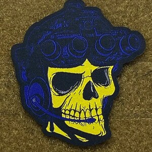 Könnte beinhalten: Ein gelber Schädel, der einen blau-schwarzen Helm mit Nachtsichtgerät und Kopfhörer trägt. Der Schädel lächelt und hat ein blaues Mikrofon im Mund.