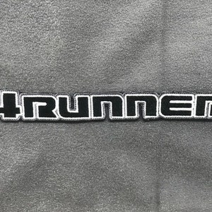 Puede incluir: Parche bordado en blanco y negro con el texto "4RUNNER" en una fuente en negrita y de bloque.