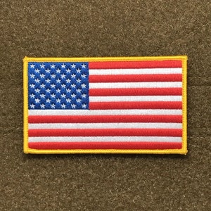 May include: A small embroidered American flag patch with a yellow border. The flag is red, white, and blue.