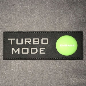 Puede incluir: Parche negro con texto blanco que dice "TURBO MODE" y un círculo verde con texto blanco que dice "ENGAGE".