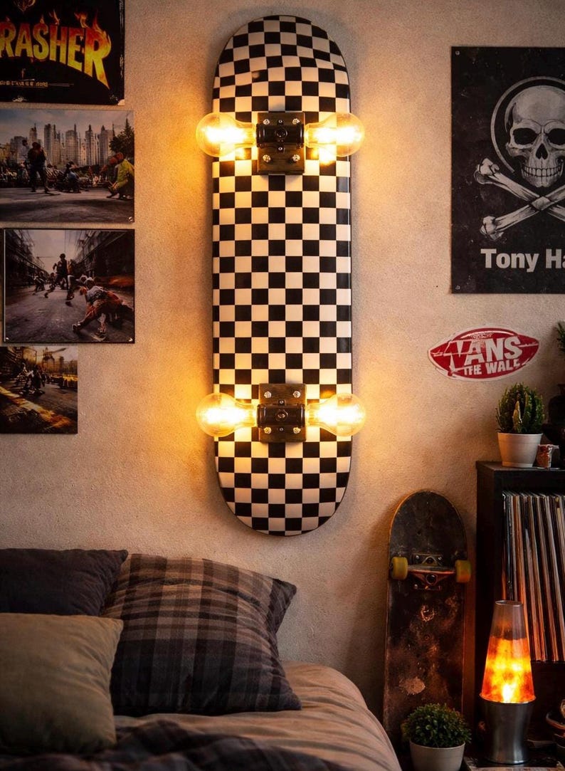 May include: A skateboard repurposed as a wall-mounted light fixture. The board features a black and white checkerboard pattern and is fitted with two Edison-style light bulbs. The fixture is mounted on a neutral-colored wall, creating a unique decor piece.