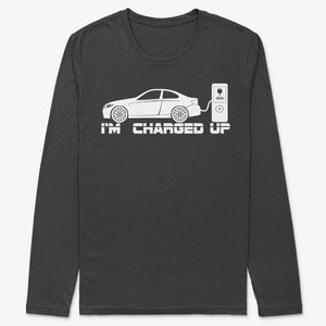 Puede incluir: Una camiseta de manga larga gris oscuro con un gráfico blanco de un coche enchufado a una estación de carga. El texto "I'M CHARGED UP" está impreso debajo del gráfico.