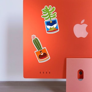 Puede incluir: Dos pegatinas de plantas coloridas sobre un fondo rojo. Una pegatina presenta un cactus en una lata con una persona que lleva una camisa roja dentro. La otra pegatina presenta una planta verde en una lata con un dise&ntilde;o azul y blanco.