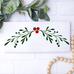 Può includere: Un cartello in legno bianco con un design a ramo di agrifoglio verde e bacche rosse. Il cartello è perfetto per aggiungere un tocco festivo alla tua decorazione domestica.