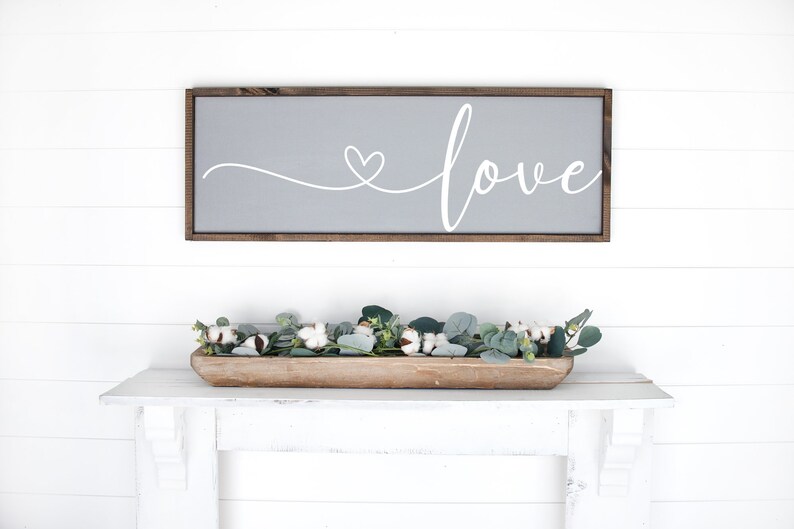 May include: A rectangular wooden sign with a grey background and the word "love" in white script, with a heart replacing the "o". Below, a wooden trough holds cotton and eucalyptus. The sign is 76 cm long.